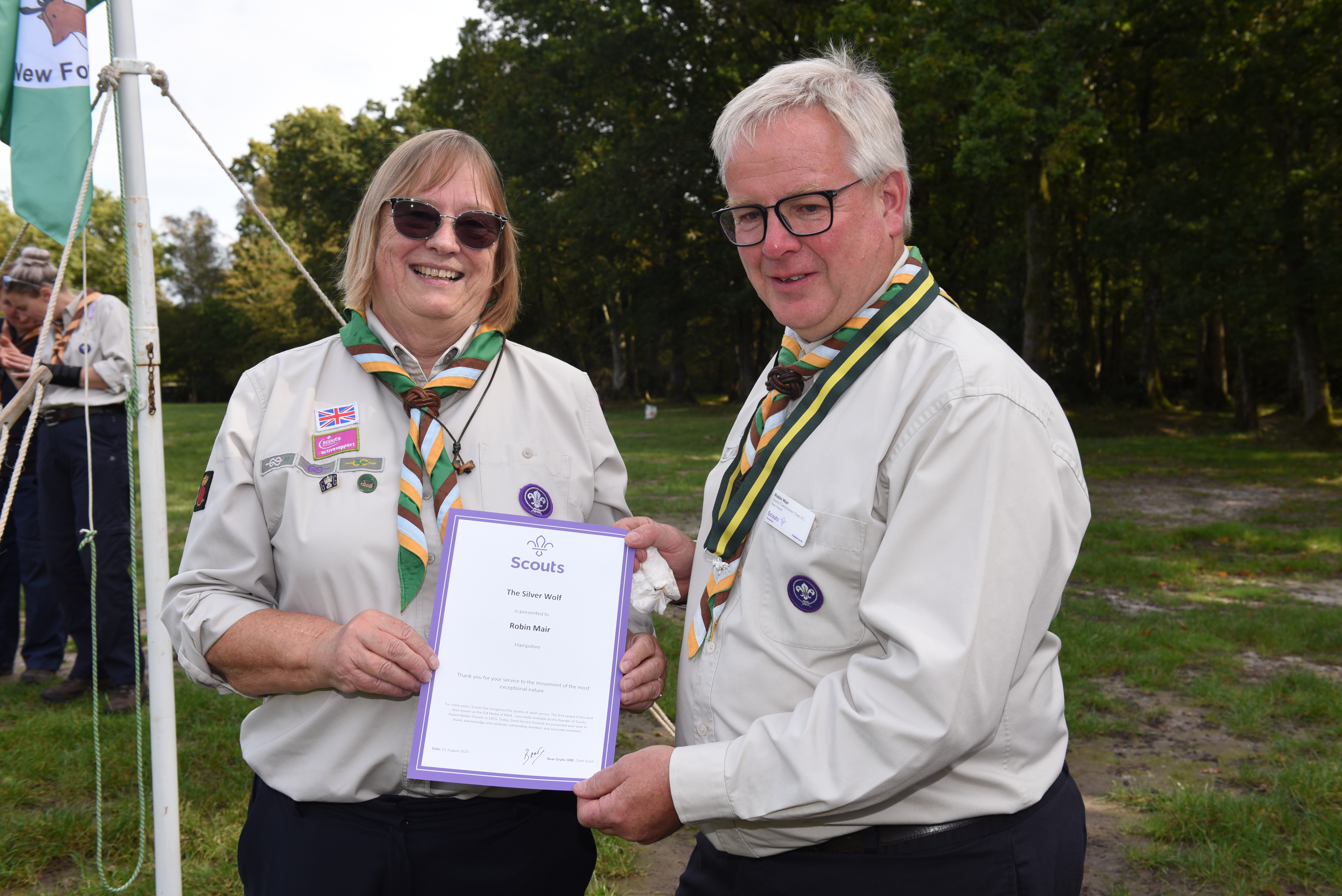 Robin Mair (r) received a certificate from Donna Kerrigan (l) at an outdoor campsite.