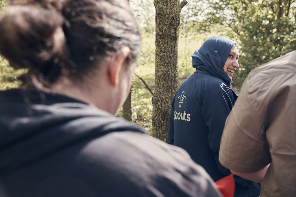 Female volunteer with a Scout jacket walking in the woods with other volunteers.